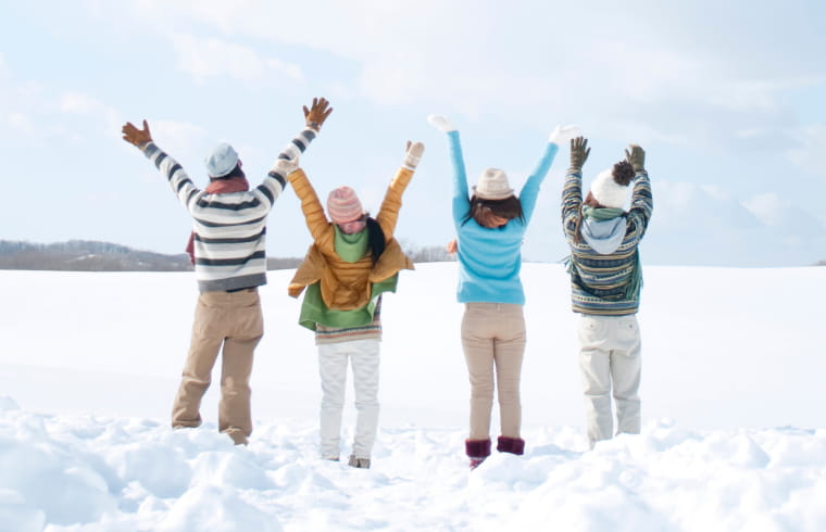 雪原で4人の人が手を上げて楽しそうにしている後ろ姿
