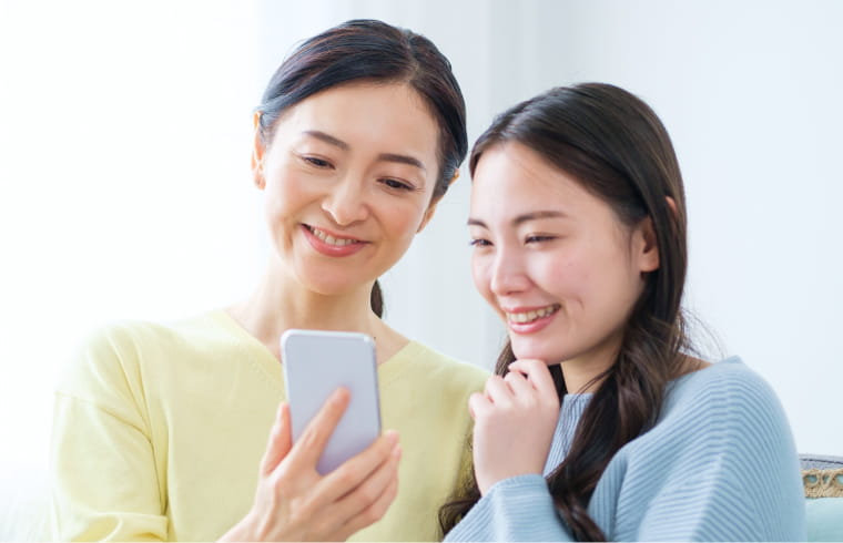 黄色と青の服を着た女性が、スマホ画面を共有している様子